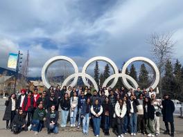 large group of students posing for a photo under the Olympic rings in Whistler village