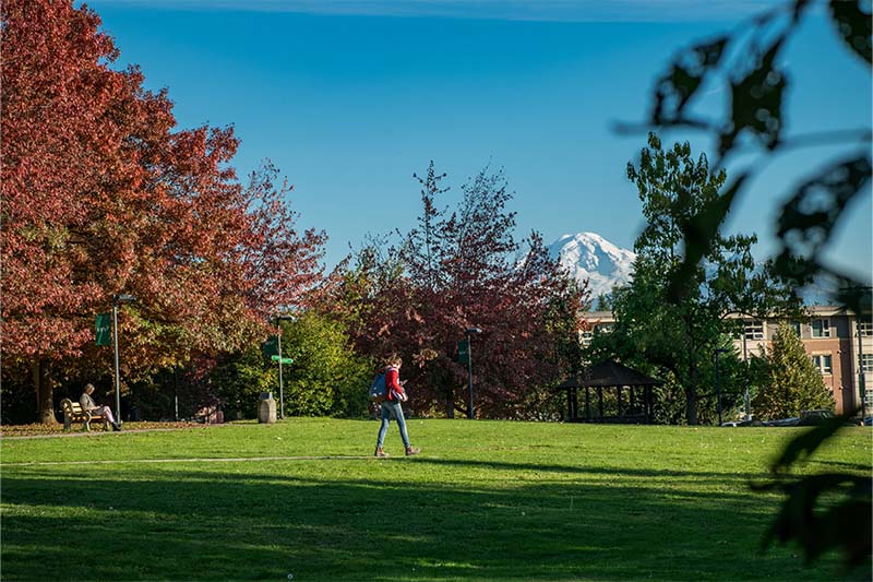 A student walks across the campus green with Mt Baker's snowy peak visible.